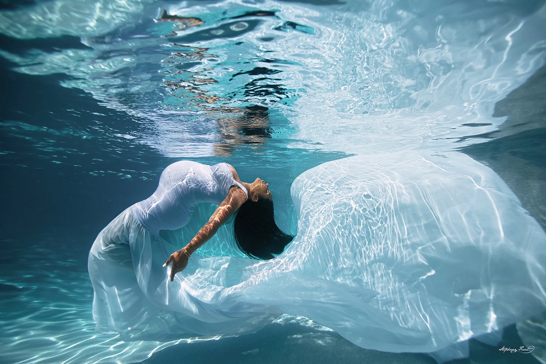 Under maternity maternity photo shoot by Stephany Ficut Photography with white gown in blue water